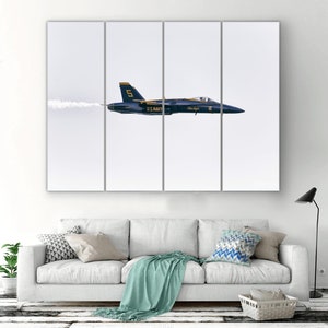 May include: A blue and yellow F/A-18 Hornet jet plane with the words "U.S. NAVY" and "Blue Angels" on the side, flying in a clear sky with a white smoke trail behind it.