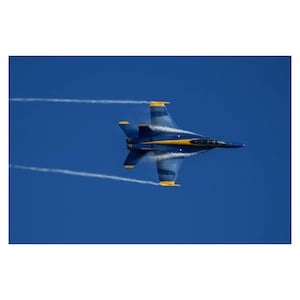 May include: A blue and yellow fighter jet flies in a clear blue sky, leaving white smoke trails behind it.