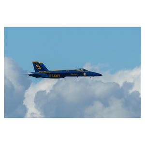 May include: A blue and yellow fighter jet with the number "5" on the tail flies through a cloudy sky. The jet is labeled "U.S. NAVY" and "Blue Angels".