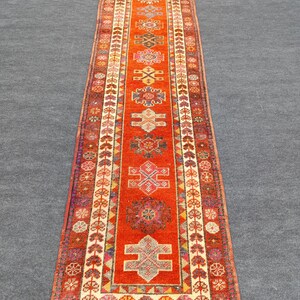 May include: A long, narrow rug with a traditional Persian design. The rug is predominantly orange with intricate patterns in shades of red, blue, and white.