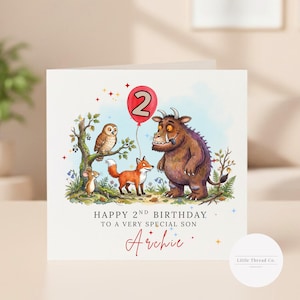 May include: A square greeting card featuring a brown monster, a fox, an owl, and a mouse in a forest setting. A red balloon with the number 2 floats above. Text reads: HAPPY 2ND BIRTHDAY TO A VERY SPECIAL SON Archie, with colorful star accents.