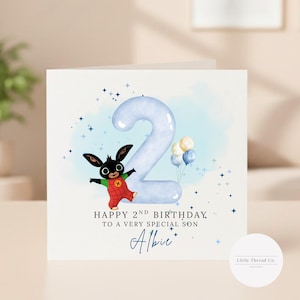May include: A square birthday greeting card featuring a large light blue number two, a cartoon rabbit character in red overalls, and a cluster of small balloons. The text reads: HAPPY 2ND BIRTHDAY TO A VERY SPECIAL SON, followed by the name Albie.