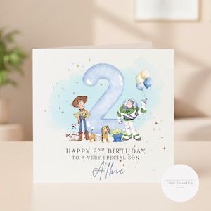May include: A birthday card with a light blue number 2 and cartoon characters. The card reads "Happy 2nd Birthday to a very special son Albie". The characters include Woody, Buzz Lightyear, and other Toy Story characters.