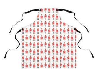 May include: White apron with a repeating pattern of red and gold toy soldiers wearing crowns. The apron has black ties and a pocket. A festive kitchen accessory.