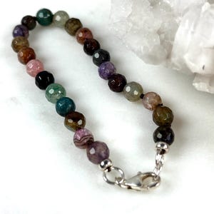 May include: A multi-colored gemstone bracelet with a silver clasp. The bracelet features a variety of colors, including pink, green, purple, and brown.