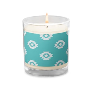 May include: A lit candle in a clear glass jar. The candle has a turquoise band with a white geometric pattern. The candle is filled with a creamy wax and has a lit wick. The candle is a decorative home accent.
