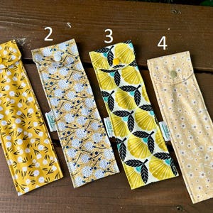 May include: Four rectangular fabric pouches with snap closures, numbered 1 through 4. Each pouch features a distinct yellow-toned pattern: white flowers, blue dandelion-like seeds, yellow and black stylized leaves, and small white daisies.