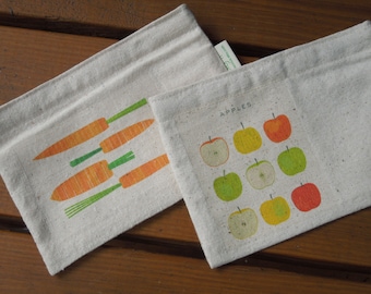 Puede incluir: Dos bolsas de lona blancas con diseños diferentes. Una bolsa tiene un estampado de zanahorias y la otra tiene un estampado de manzanas con la palabra "Manzanas" encima.