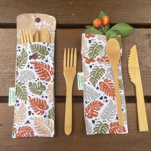 May include: Two bamboo utensil sets with leaf-patterned fabric cases. One case is open, revealing a fork, spoon, and knife. The other case holds a fork, spoon, and knife. The cases have a beige top with a button closure.