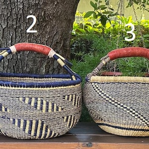May include: Four woven baskets labeled 1, 2, 3, and 4, each featuring a round body, a dark blue rim, and a wrapped red handle. The baskets display various geometric patterns in natural tan and dark brown fibers, arranged in a row.