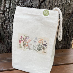 May include: A white canvas lunch bag with a floral print and a green circle logo that says "EST. 1985 ECO BAGS".