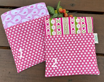 Könnte beinhalten: Zwei wiederverwendbare Einkaufstaschen in Pink mit weißen Punkten. Die Oberseite jeder Tasche hat ein anderes Muster. Eine Tasche hat ein pinkfarbenes und weißes Vogelmuster und die andere ein pinkfarbenes, grünes und weißes Blumenmuster. Die Taschen sind mit 1 und 2 nummeriert.