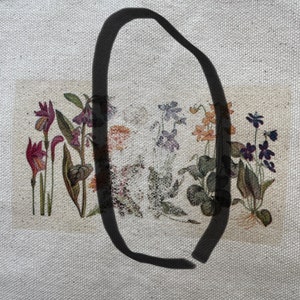 May include: A close-up of a white canvas tote bag with a black oval drawn on it. The bag has a printed image of a row of colorful flowers with green leaves.