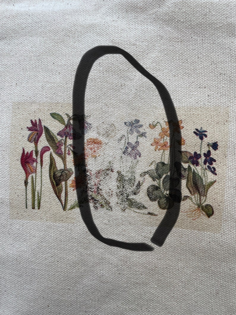 May include: A close-up of a white canvas tote bag with a black oval drawn on it. The bag has a printed image of a row of colorful flowers with green leaves.