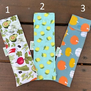 May include: Three reusable utensil cases with different patterns. The first case has a white background with a green, red, and black vegetable pattern. The second case has a light blue background with a yellow lemon pattern. The third case has a light blue background with a yellow and orange fruit pattern.