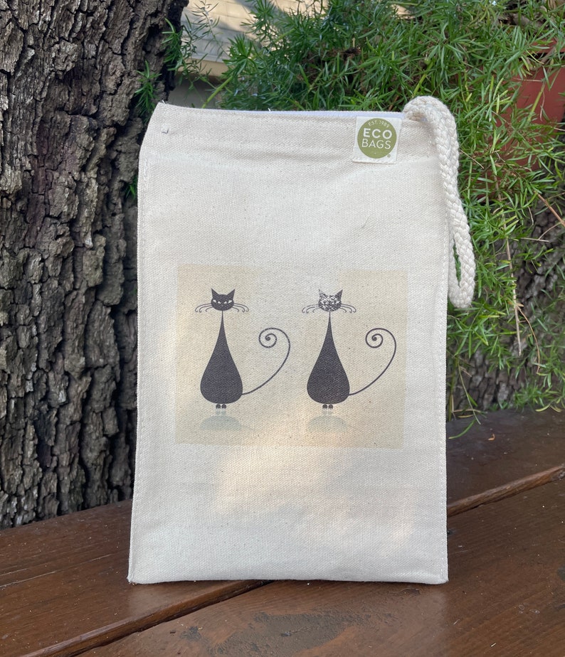 May include: A white canvas tote bag with black cats and the text "Eco Bags" printed on the front. The bag has a drawstring closure.