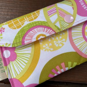 May include: A colorful fabric pouch with a floral and geometric pattern in pink, yellow, and green on a white background. The pouch is closed with a pink button. The tag reads "Bag it" and "bagitconscious.etsy.com".
