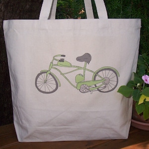 May include: A white canvas tote bag with a green bicycle illustration printed on the front. The bicycle has a black seat and a brown handlebar.