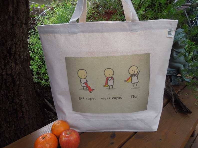 May include: A white canvas tote bag featuring a graphic of three stick figures wearing capes. The text on the bag reads "get cape. wear cape. fly."