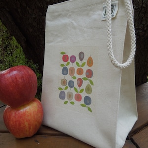 Puede incluir: Una bolsa de lona blanca con un dise&ntilde;o de frutas y hojas de colores. La bolsa tiene un asa larga de cuerda blanca.