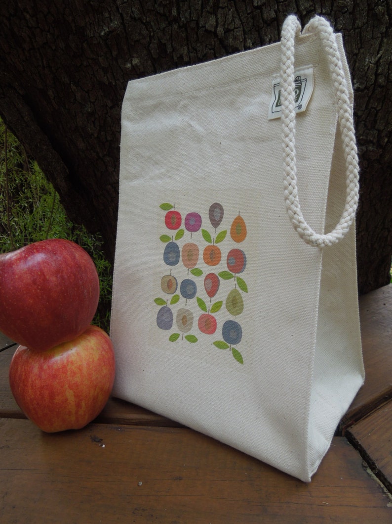 Puede incluir: Una bolsa de lona blanca con un dise&ntilde;o de frutas y hojas de colores. La bolsa tiene un asa larga de cuerda blanca.