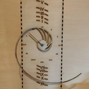 Może przedstawiać: Drewniany zegar z rzymskimi cyframi oznaczającymi godziny. Tarcza zegara jest okrągła i ma spiralny wzór. Zegar wykonany jest z jasnego drewna i ma ciemną drewnianą ramkę.