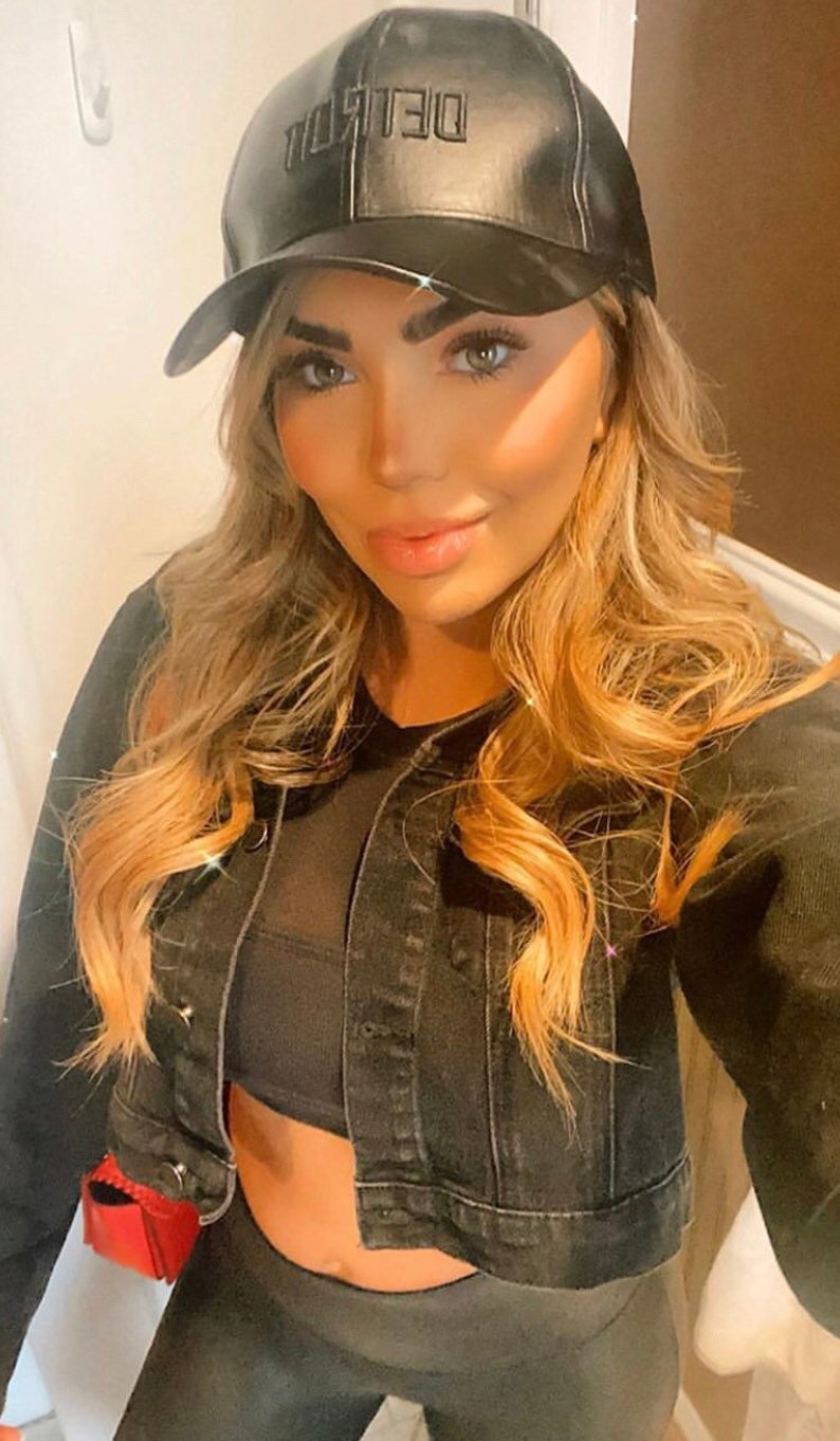 K&ouml;nnte beinhalten: Schwarze Baseballkappe aus Leder mit "DETROIT" auf der Vorderseite gestickt. Die Kappe wird mit einer schwarzen Jeansjacke und schwarzen Leggings getragen. Das Bild hat einen warmen, gefilterten Ton.