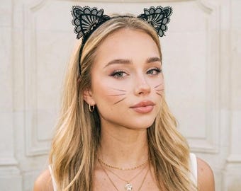 Puede incluir: Una diadema negra con dos orejas de gato erguidas, confeccionadas en encaje delicado e intrincado con un diseño de borde festoneado. Las orejas de encaje están montadas sobre una banda negra fina y flexible que se ajusta a la cabeza.