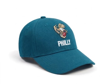 May include: A teal baseball cap featuring an embroidered graphic of an eagle clutching a red football. Below the eagle, the word PHILLY is embroidered in white capital letters. The cap has a structured crown, a curved brim, and eyelet vents.