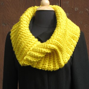 May include: A bright yellow crocheted cowl neck scarf on a black coat.