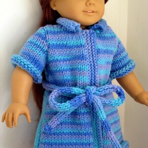 May include: A blue and purple striped knitted robe with a tie belt. The robe is designed for a doll.