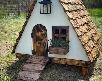 Könnte beinhalten: Ein charmantes, handgefertigtes Holzspielhaus mit Schindeldach, gewölbter Tür und kleinem Fenster. Die weißen Wände kontrastieren mit den natürlichen Holztönen der Tür, des Fensterrahmens und der Rampe. Über der Tür hängt eine schwarze Laterne.