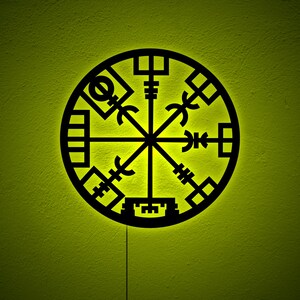 Op de afbeelding: Een zwarte metalen wanddecoratie met een cirkelvormig ontwerp met een kompasachtig symbool met acht punten. Het symbool wordt omringd door een cirkel met geometrische patronen.