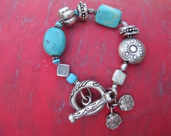 May include: A turquoise and silver bracelet with a decorative clasp. The bracelet features various turquoise stones and silver beads, including a large round bead with a floral design.