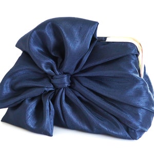 May include: A navy blue satin clutch bag with a large bow on the front.