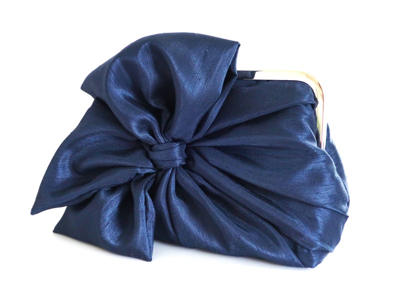 May include: A navy blue satin clutch bag with a large bow on the front.