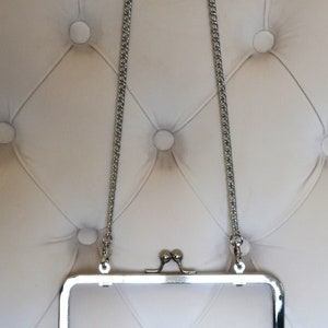 May include: Silver metal purse frame with a chain strap. The frame is open and the chain is hanging down.