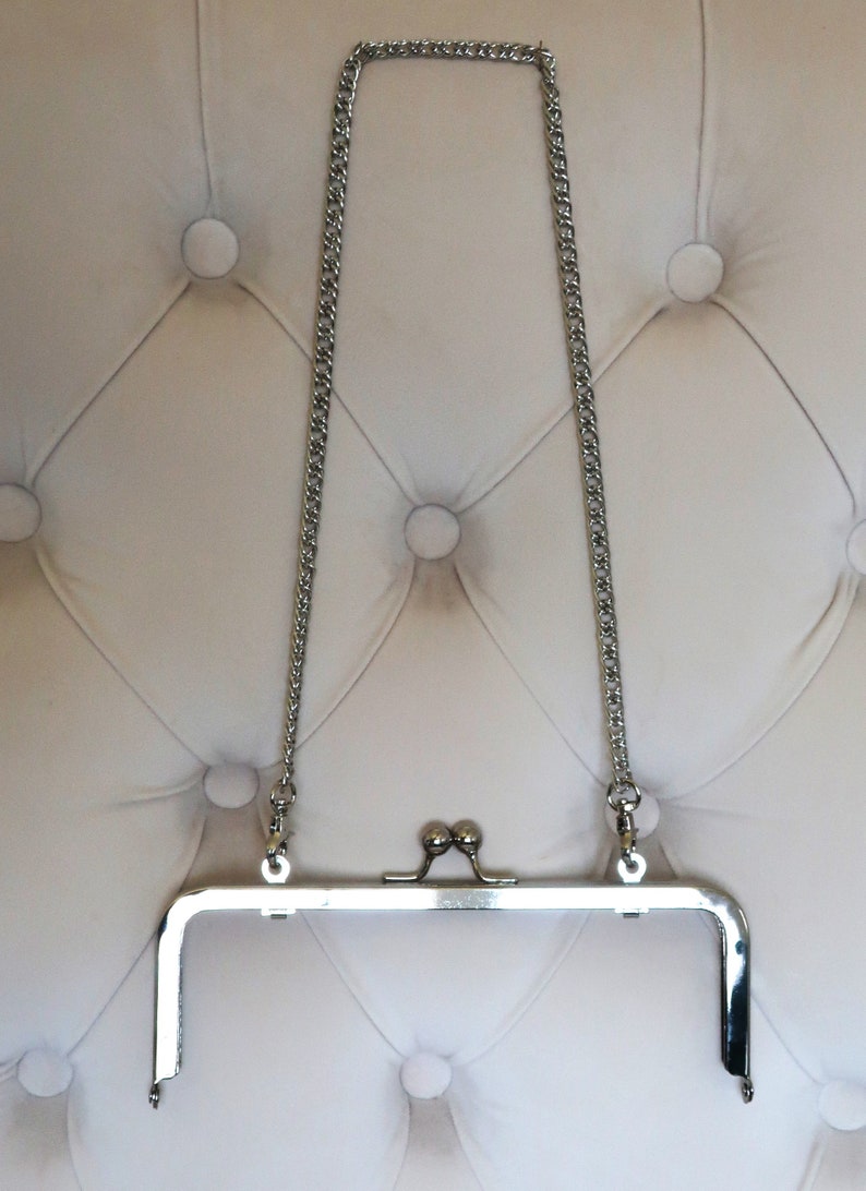 May include: Silver metal purse frame with a chain strap. The frame is open and the chain is hanging down.