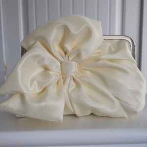 May include: A white satin clutch bag with a large bow on the front.