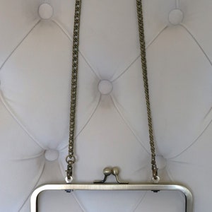May include: A gold-toned metal purse frame with a chain strap. The frame is open and the chain is hanging down.