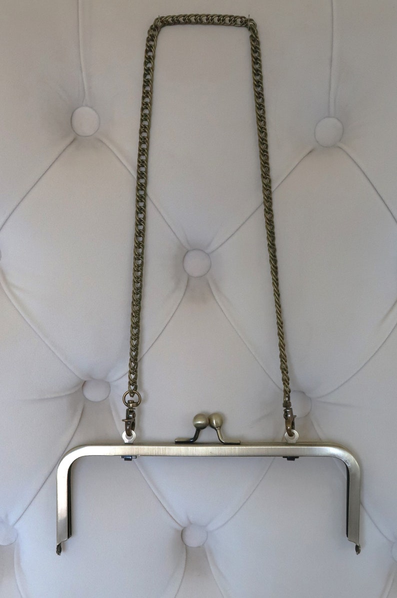 May include: A gold-toned metal purse frame with a chain strap. The frame is open and the chain is hanging down.