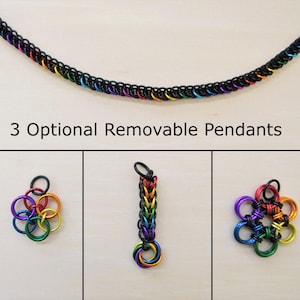 May include: A chain necklace constructed from black metal rings interspersed with rainbow-colored rings. The text 3 Optional Removable Pendants is displayed above three distinct pendant designs made from matching black and rainbow metal rings.