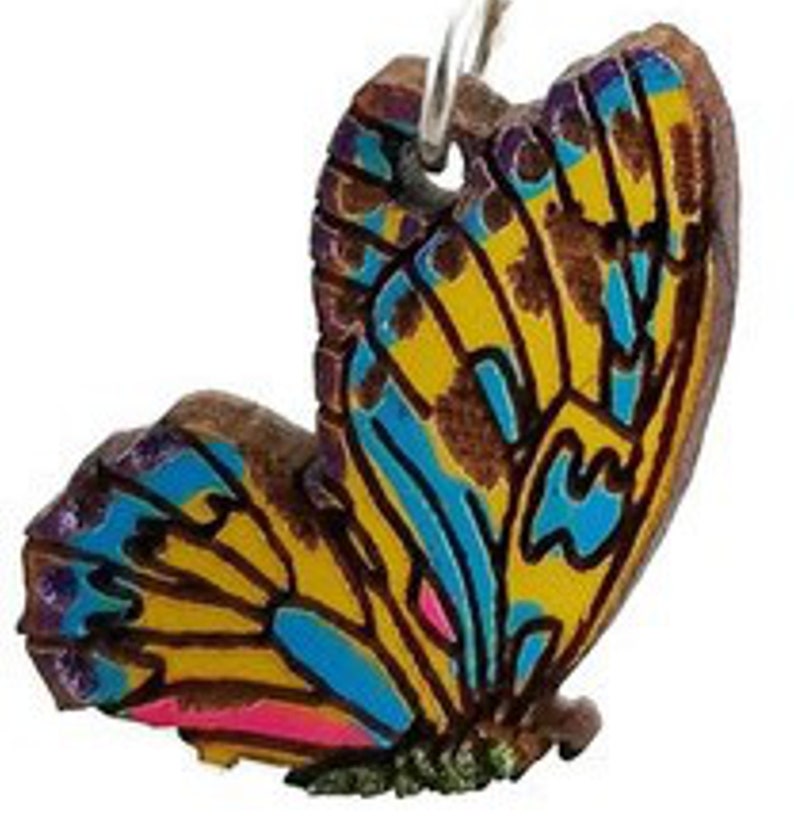 K&ouml;nnte beinhalten: Ein Schmetterlingsanh&auml;nger mit aufwendigen Details. Die Fl&uuml;gel zeigen ein lebendiges Muster aus Gelb, Blau und Rosa auf braunem Hintergrund. Der Anh&auml;nger h&auml;ngt an einer silberfarbenen Schlaufe.