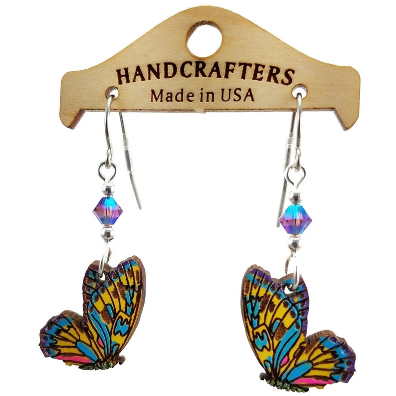 K&ouml;nnte beinhalten: Schmetterlingsohrringe mit silberfarbenen Haken und schillernden Kristallperlen. Die Holz-Schmetterlingsanh&auml;nger haben gelbe, blaue und rosa Fl&uuml;geldesigns. Die Ohrringe werden auf einem Holzschild mit der Aufschrift "HANDCRAFTERS Made in USA" pr&auml;sentiert.