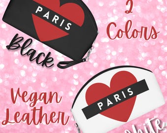 Può includere: Due trousse da trucco in pelle vegana con un design a forma di cuore e la scritta "PARIS" stampata su di esse. Una borsa è nera e l'altra è bianca.