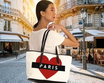 Può includere: Borsa tote bianca con un cuore rosso e la parola "PARIS" in lettere nere. La borsa ha manici neri e un bordo nero.