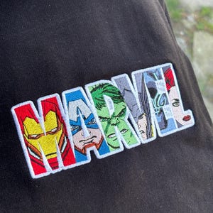 May include: Black sweatshirt with an embroidered "MARVEL" logo featuring Iron Man, Captain America, Hulk, Thor, and Scarlet Witch.