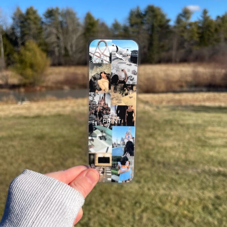 Pu&ograve; includere: Un segnalibro di plastica trasparente con un collage di foto. Le foto includono una montagna russa, un castello, una coppia e una donna con un vestito blu. Il testo "The Print" &egrave; visibile sul segnalibro.