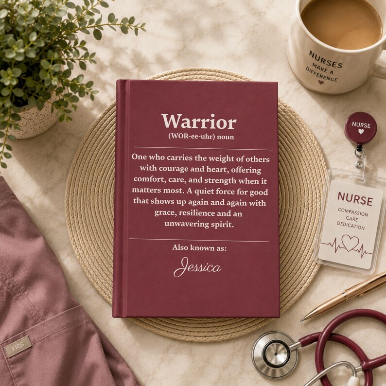 Op de afbeelding: Een bordeauxrood hardcover boek met de definitie van het woord Warrior, dat iemand beschrijft die de last van anderen met moed en hart draagt, inclusief de naam Jessica onderaan. Het boek ligt op een ronde, gevlochten onderzetter.