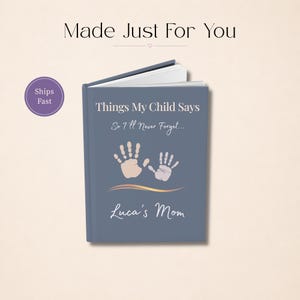 May include: A blue hardback journal with the text Things My Child Says So I'll Never Forget and Luca's Mom printed on the front cover. The cover features two light-coloured handprint illustrations and a gold-toned wavy line graphic element.